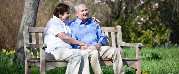 Carer sitting on garden bench with elderly man receiving dementia care