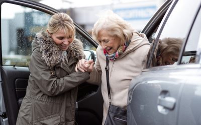 A mature woman helps a senior woman out of a car as she takes her to the shops