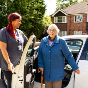 Care professional helping elderly lady out of car