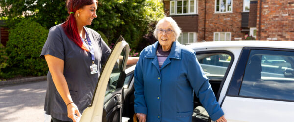 Care professional helping elderly lady out of car